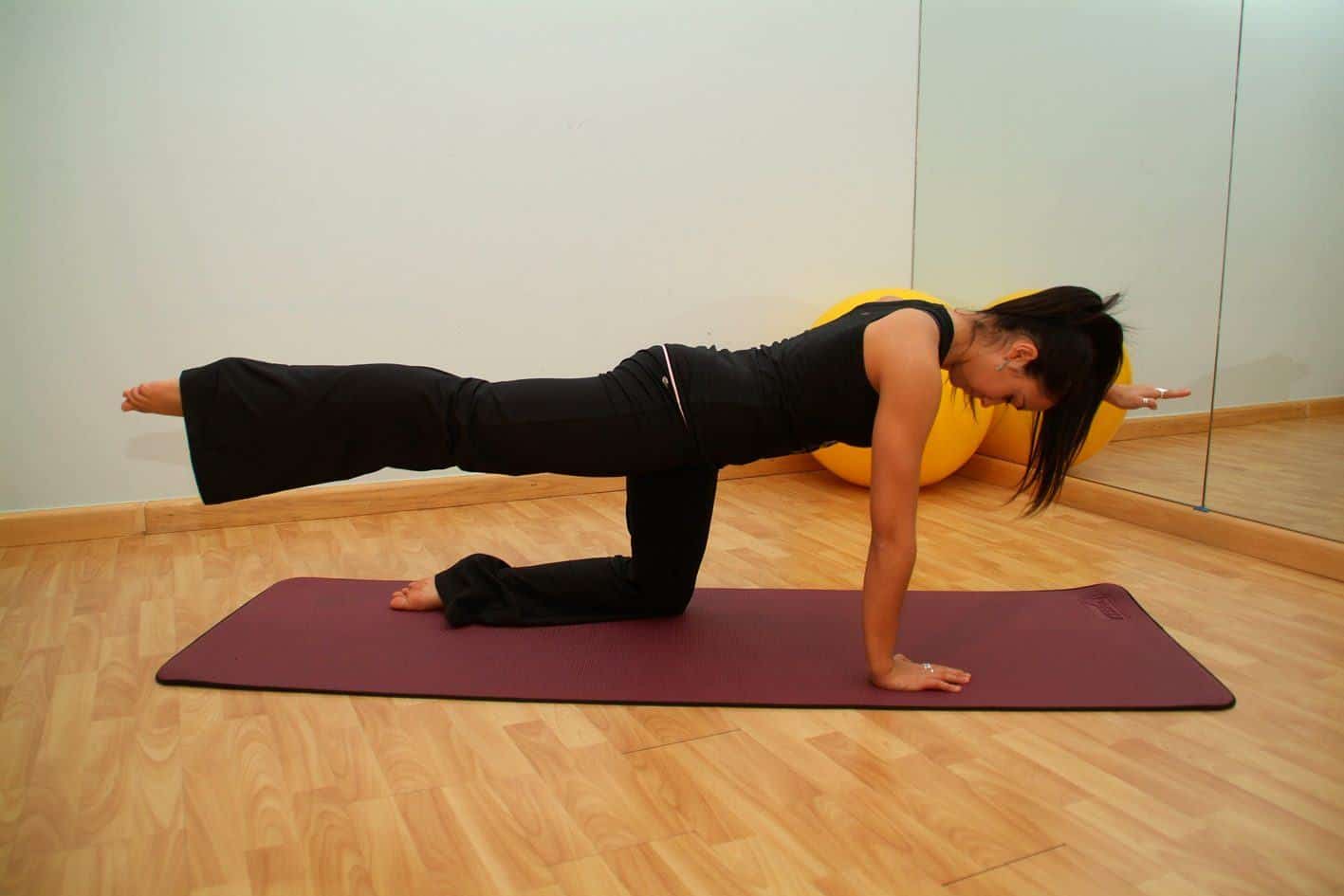 A woman on all fours on a mat extending one leg behind her in a studio