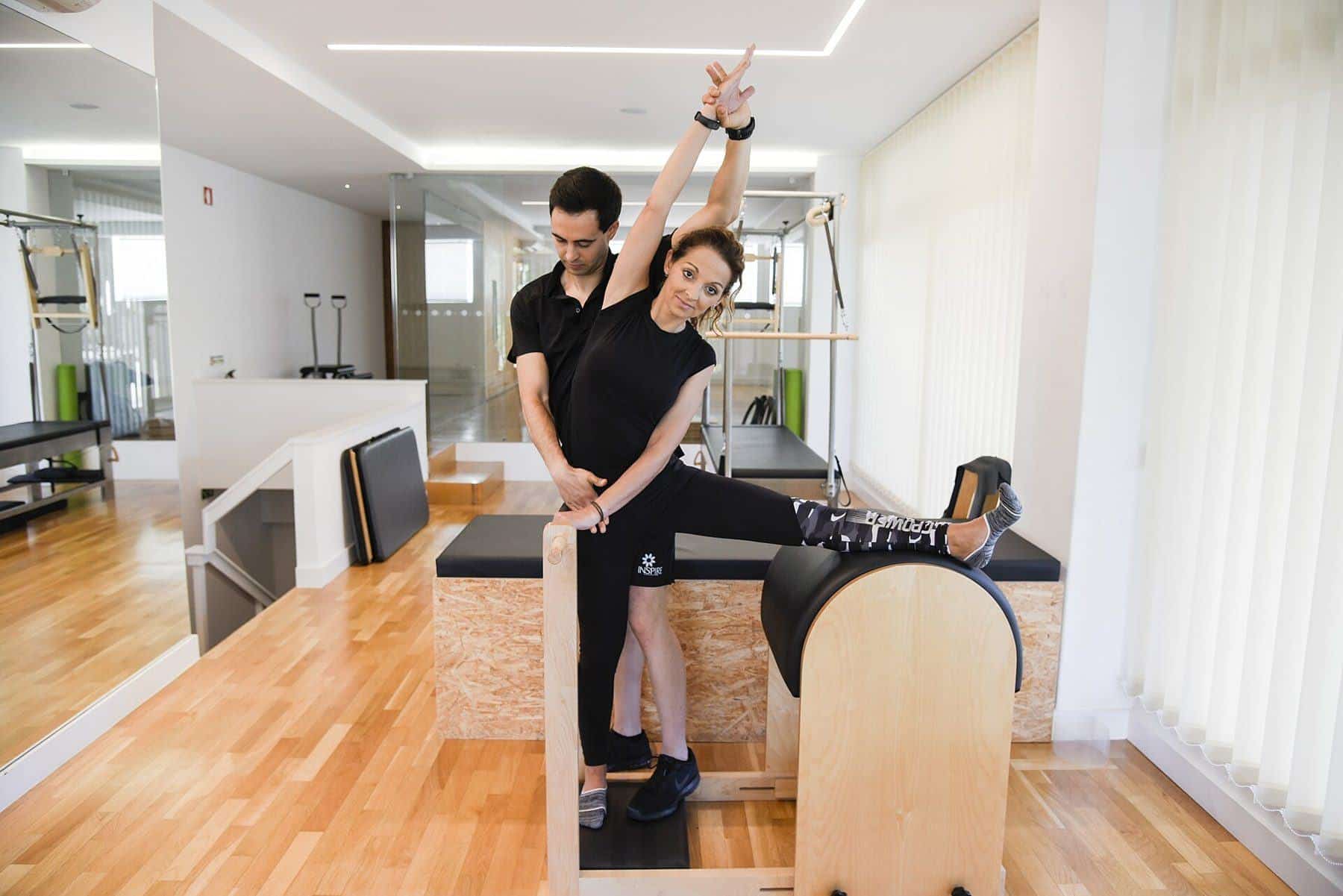 An instructor supporting a woman on a ladder barrel in a fully equipped Pilates studio